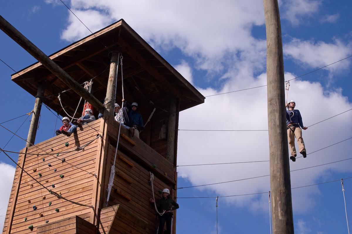 在新葡京平台，学生们坐在岩壁上的高绳索课程塔上